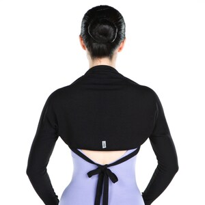 May include: A black long-sleeved shrug with a tie in the back. The shrug is worn over a light purple sleeveless dress.