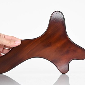 Pode incluir: Uma ferramenta de gua sha de madeira marrom com um formato único, projetada para massagem e relaxamento.
