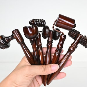 Könnte beinhalten: Ein Set aus sechs dunkelbraunen hölzernen Massagegeräten mit glatten, polierten Griffen. Das Set enthält verschiedene Formen wie geriffelte Rollen, eine glatte zylindrische Rolle und abgerundete Köpfe für die manuelle Körpermassage.