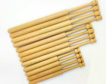 May include: A set of 12 wooden bobbins for lace making. The bobbins are natural wood color and have a smooth finish. They are arranged in a staggered pattern, with the largest bobbin at the top and the smallest at the bottom.