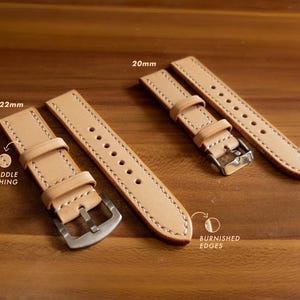 May include: Two leather watch straps in a light brown color with white stitching. The strap on the left is 22mm wide and the strap on the right is 20mm wide. Both straps have burnished edges and saddle stitching.