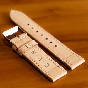 May include: Two light brown leather watch straps with white stitching. The strap on the bottom has the text "C.A.R." embossed on it.