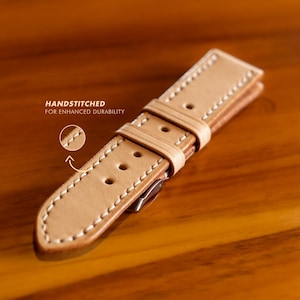 May include: A light brown leather watch strap with white stitching. The strap is handstitched for enhanced durability.