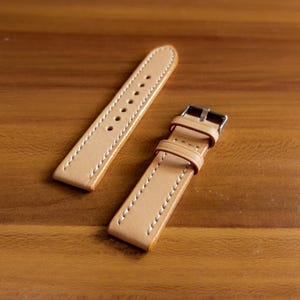 May include: Two light brown leather watch straps with white stitching. One strap has a metal buckle.