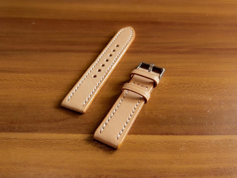 May include: Two light brown leather watch straps with white stitching. One strap has a metal buckle.