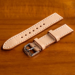 May include: Two light brown leather watch straps with white stitching. One strap has a silver buckle.