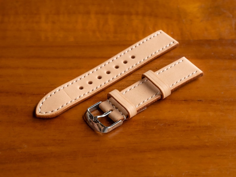 May include: Two light brown leather watch straps with white stitching. One strap has a silver buckle.