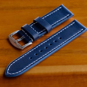 May include: A dark blue leather watch strap with white stitching and a silver buckle.