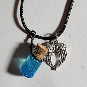 May include: A necklace with a small glass bottle containing blue liquid and a silver-coloured angel wing charm. The bottle has a cork stopper and is on a black cord. The angel wing charm is detailed.