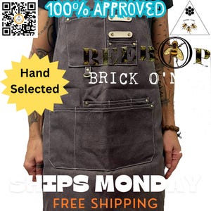 May include: A gray denim apron with a large pocket and two smaller pockets. The apron has a white stitched border and the text "BEEF  BRICK O'N" in yellow letters. The text "100% APPROVED" is in white letters on a black rectangle at the top of the apron.