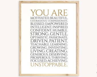 Puede incluir: Una impresión enmarcada con un texto dorado superpuesto sobre un fondo blanco. El texto dice "You Are" seguido de una lista de atributos positivos, que incluyen "Motivated, Beautiful, Courageous, Compassionate, Blessed, Empowered, Intelligent, Inspired, Confident, Humble, Strong, Gentle, Optimistic, Passionate, Driven, Patient, Teachable, Learning, Growing, Inventing, Living, Creating, Generous, Deserving, Prosperous, Thriving, Focused, Achieving, Unstoppable."
