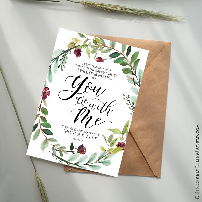 K&ouml;nnte beinhalten: Eine Gru&szlig;karte mit dem Text "You are with Me" in eleganter Schrift, umgeben von einem Aquarell-Blumenkranz aus gr&uuml;nen Bl&auml;ttern und burgunderfarbenen Bl&uuml;ten. Die Karte wird mit einem braunen Umschlag pr&auml;sentiert.