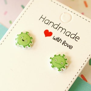 May include: A pair of green and white cartoon virus stud earrings on a white card with the text "Handmade with love".