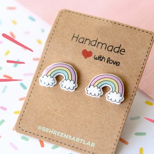 K&ouml;nnte beinhalten: Ohrstecker in Regenbogenform auf einer braunen Karte mit dem Text "Handmade with love". Die Ohrringe haben Pastellfarben und wei&szlig;e Wolken. Die Karte befindet sich auf einem Hintergrund mit bunten Konfetti.
