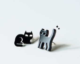 May include: A pair of black cat stud earrings. One cat is sitting and the other is standing with its tail up.