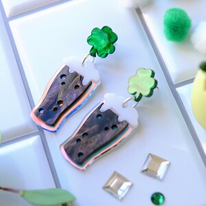 May include: A pair of iridescent green and white acrylic earrings shaped like a pint of beer with a shamrock charm.
