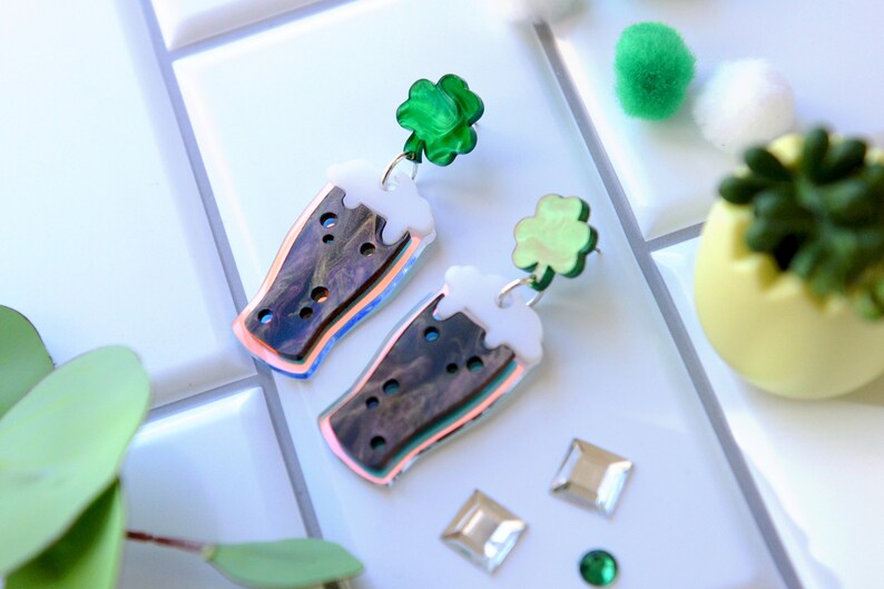 May include: A pair of iridescent green and white acrylic earrings shaped like a pint of beer with a shamrock charm.