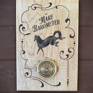 May include: A wooden sign with a black and white illustration of a horse and the text "The Mare Barometer". The sign also features a round, gold-colored barometer with a needle pointing to "Fair" weather.