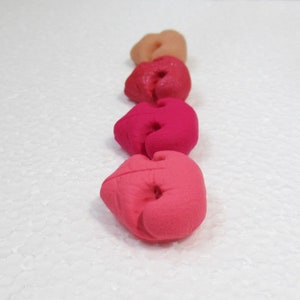 May include: Five heart-shaped clay beads in shades of pink, red, and peach. The beads are arranged in a row from lightest to darkest.