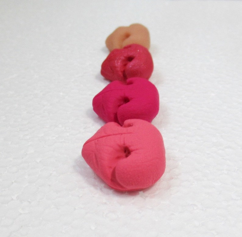 May include: Five heart-shaped clay beads in shades of pink, red, and peach. The beads are arranged in a row from lightest to darkest.