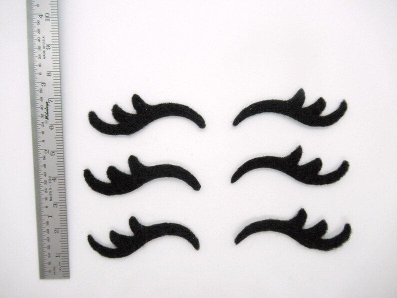 May include: Six black felt eyelashes, each with a unique shape and curve, ideal for crafting or decorating.