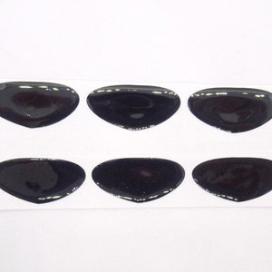 Peut inclure: Six autocollants ovales noirs sur une feuille de papier blanche. Les autocollants sont brillants et ont un léger éclat.