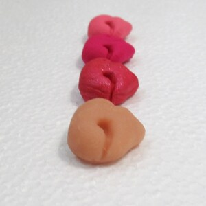 May include: Four heart-shaped clay pieces in shades of pink, red, and orange. The pieces are arranged in a row from lightest to darkest.
