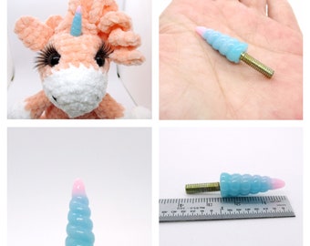 May include: A pink and blue unicorn horn charm with a gold screw thread. The horn is about 1.5 inches long and is made of a soft, pliable material.