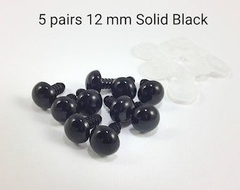 Puede incluir: Diez ojos de seguridad de plástico negro con tornillo de cierre, que miden 12 mm de diámetro. Los ojos están dispuestos en un grupo sobre una superficie blanca. El texto "5 pares 12 mm Sólido Negro" es visible sobre los ojos.
