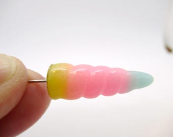 May include: A single earring featuring a yellow, pink, and blue swirl design. The earring is made of resin and has a silver post.