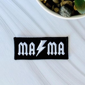 May include: Black iron-on patch with white embroidered text that reads "MA⚡️MA".
