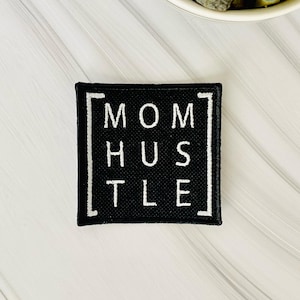 May include: Black square patch with white text that reads "MOM HUSTLE" in a bold, sans-serif font.