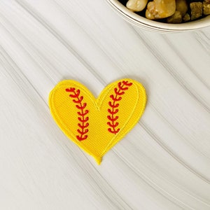 May include: A yellow heart-shaped patch with red stitching, resembling a softball.