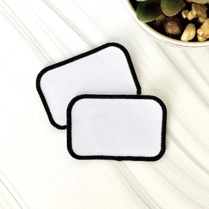 May include: Two white iron-on patches with black borders. The patches are rectangular and are on a white surface.
