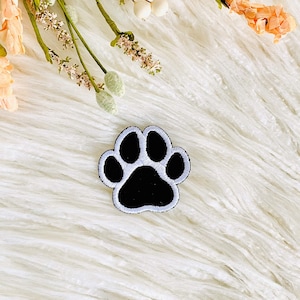 May include: Black paw print iron-on patch with white stitching on a white fluffy background.