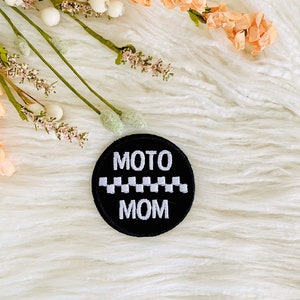 May include: Black and white embroidered patch with the text "MOTO MOM" and a checkered stripe.