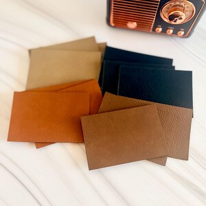 May include: A collection of rectangular leather swatches in various shades of tan, brown, and black, featuring a visible grain texture. A small, black, vintage-style radio with copper-coloured accents is positioned above the leather samples.