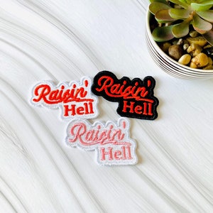 May include: Three iron-on patches with the text "Raisin' Hell" in red embroidery on a white, black, and pink background.