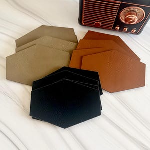 May include: A collection of hexagonal coasters in black, tan, and brown with a textured finish, arranged in three overlapping stacks. A small black and copper-colored vintage-style radio with a circular dial sits in the upper right corner.
