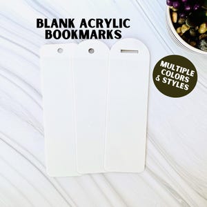 May include: Three blank white acrylic bookmarks with rounded edges and a hole at the top. The bookmarks are on a white marble surface. The text "BLANK ACRYLIC BOOKMARKS" is at the top of the image. The text "MULTIPLE COLORS & STYLES" is in a brown circle at the bottom right of the image.