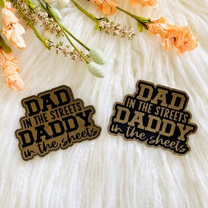 May include: Two brown paper stickers with black text. The text on the stickers reads "Dad in the streets Daddy in the sheets".