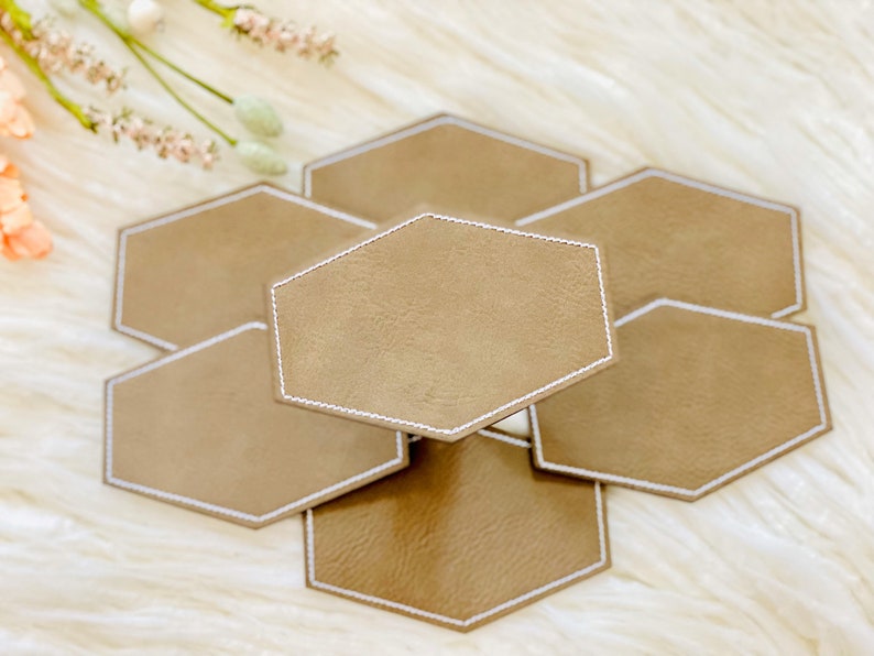 Pode incluir: Conjunto de seis  tapetes de couro marrom hexagonais com costuras brancas. Os tapetes est&atilde;o empilhados uns sobre os outros.