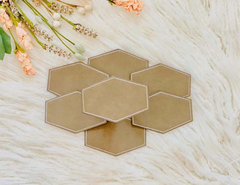 Pode incluir: Conjunto de seis  tapetes de copo hexagonal de cor castanho claro com costuras brancas ao redor das bordas. Os tapetes de copo est&atilde;o dispostos em forma de favo de mel.