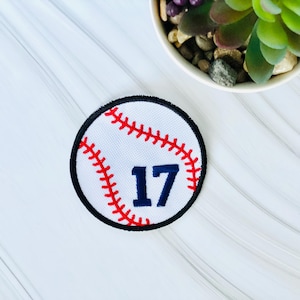 May include: White baseball patch with red stitching and a blue number 17 in the center.