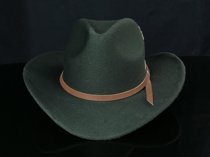 May include: A dark green felt cowboy hat with a brown leather band and a brown leather strap.