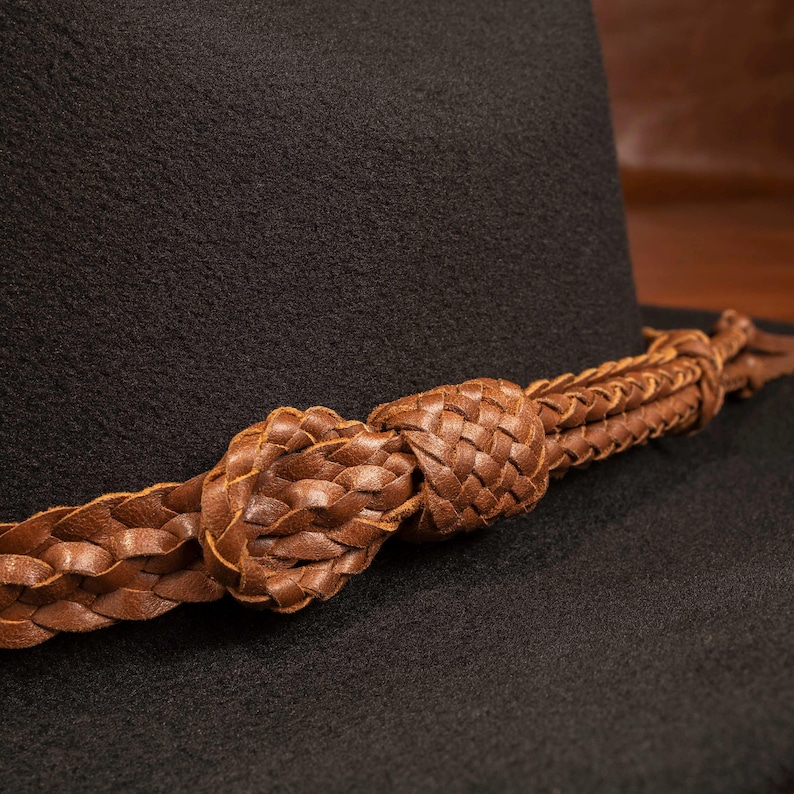 Close-up of a whiskey-brown woven leather hat band and decorative knot on a dark felt hat
