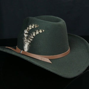 May include: A dark green felt cowboy hat with a brown leather band and a white feather accent.