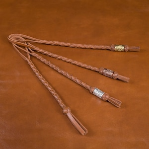 May include: Four brown leather braided lanyards with decorative metal beads. Each lanyard has a tassel at the end.