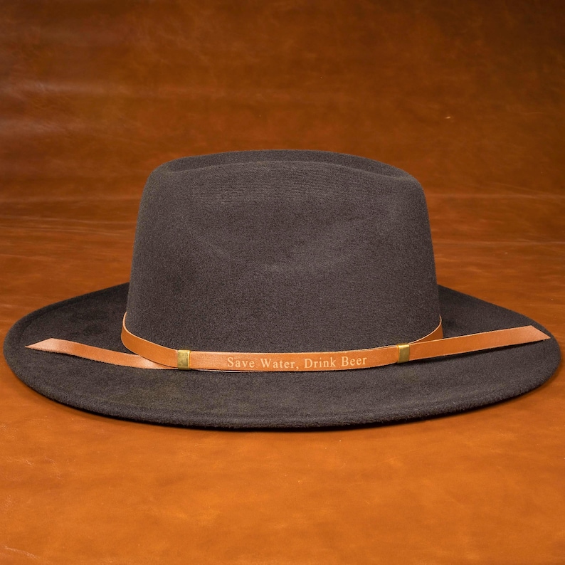 Brown leather hat band with custom engraved text on a gray Western hat