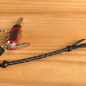 Puede incluir: Un cuchillo multiusos de bolsillo rojo y plateado con un cordón de cuero negro. El cuchillo tiene un sacacorchos, una hoja y otras herramientas.